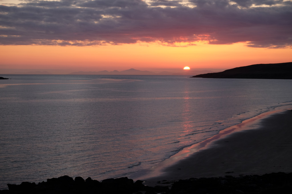 The sun “falls” behind the Isle of Skye, as seen from Gairloch. The ocean is very calm.